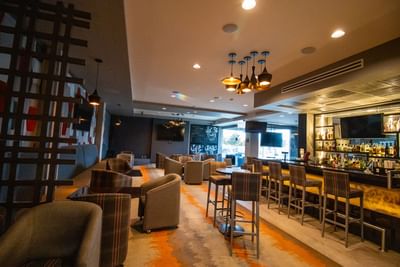 Wide view of El Colorado Bar featuring tall barstools lined by a long counter near large windows at Hotel Mirra