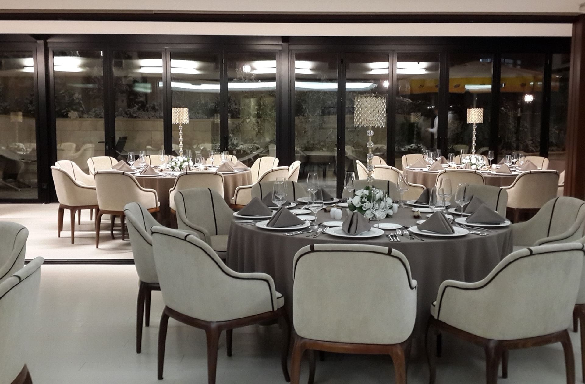 Plush chairs surrounding round tables with tall crystal lamps in a banquet hall at Warwick Ankara