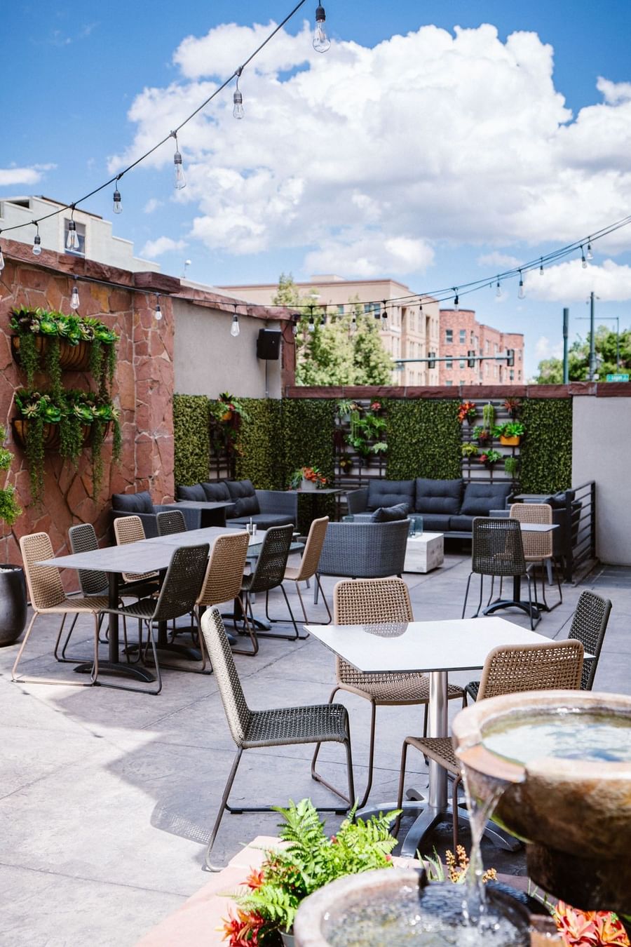 Stone patio with wicker chairs by tables under string lights near a green wall at Warwick Denver