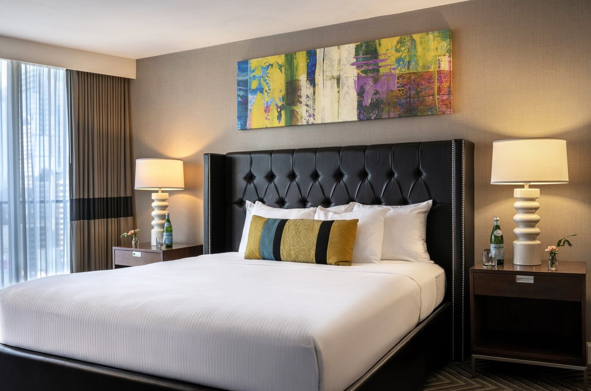 King bed with a black headboard by a colorful painting and city view windows in Emerald Suite at Warwick Seattle