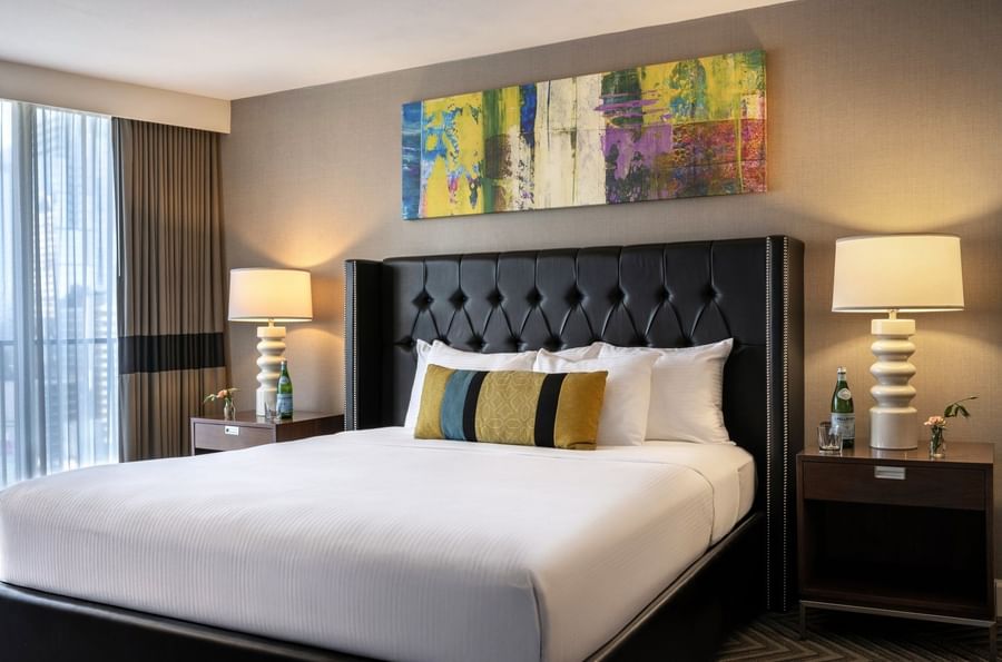 White bed with colorful pillows by modern lamps under a bright abstract painting in Queen Anne Suite at Warwick Seattle