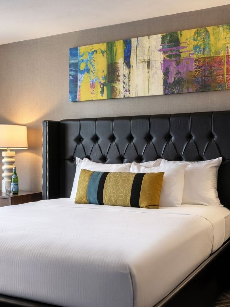 White bed with colorful pillows by modern lamps under a bright abstract painting in Queen Anne Suite at Warwick Seattle