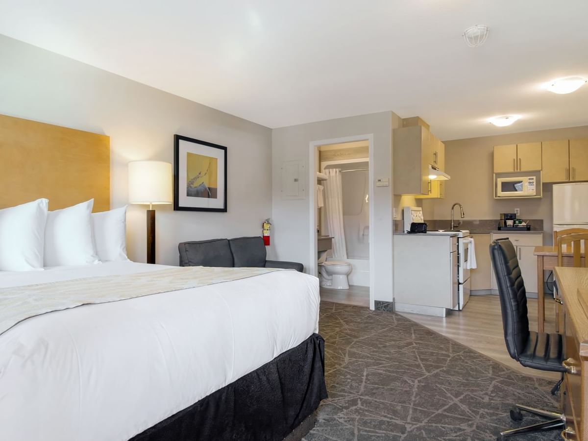 A spacious room with a queen bed, a couch, a desk, a kitchenette, and a bathroom area. 