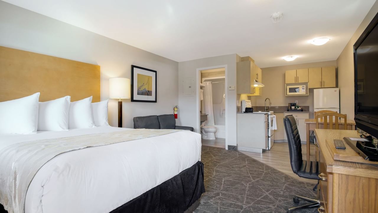 A spacious room with a queen bed, a couch, a desk, a kitchenette, and a bathroom area. 