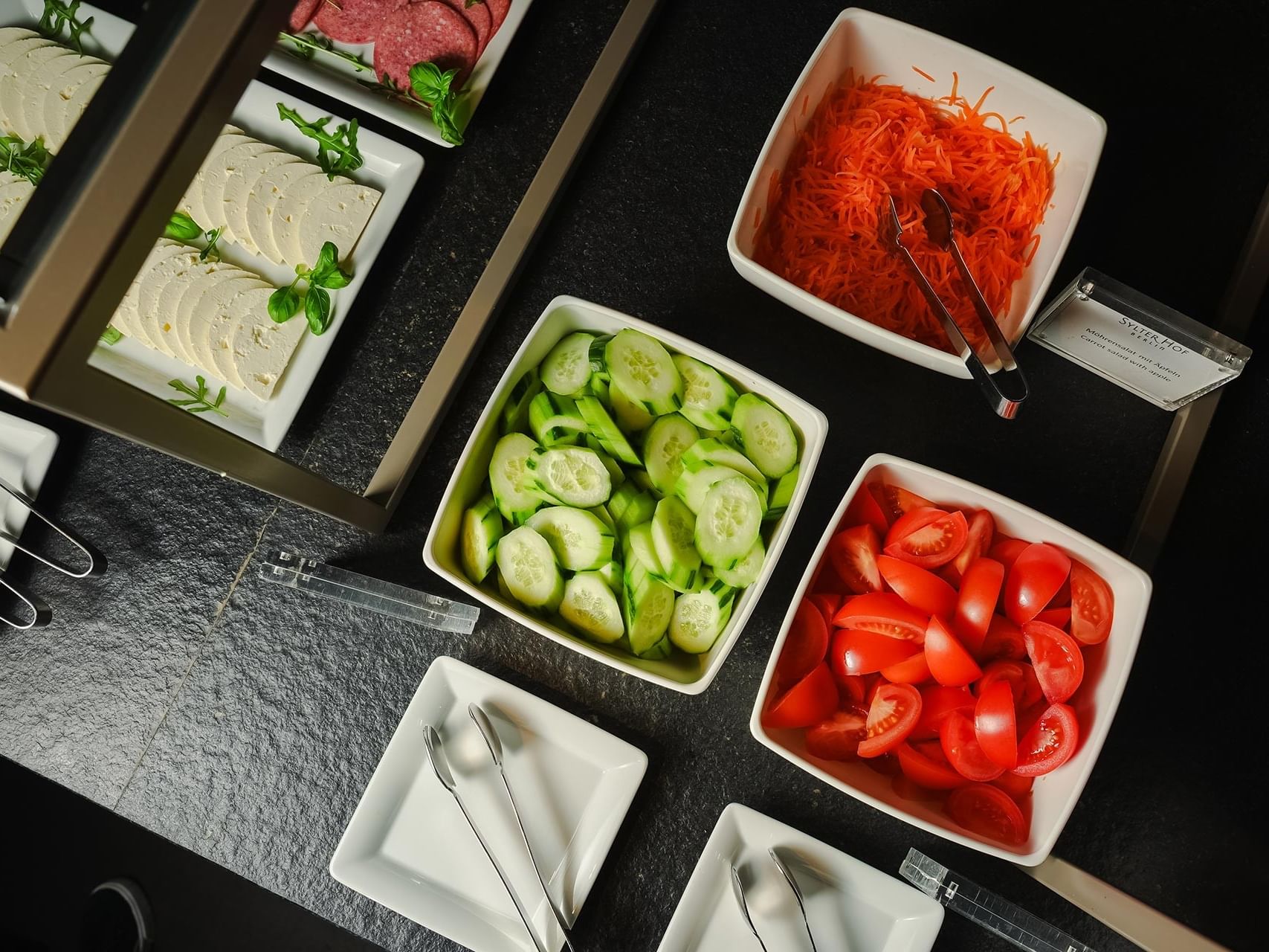 Assorted fresh vegetables in bowls and plates with tongs at Sylter Hof Berlin.
