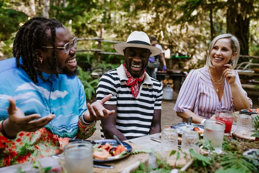 Three people laughing and enjoying meals outdoors at Alderbrook Resort & Spa