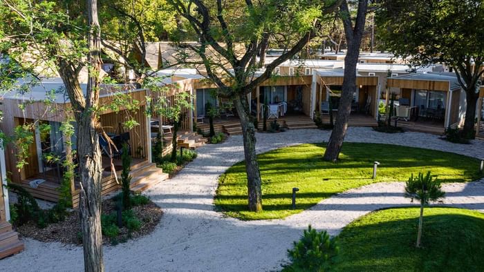 Luftaufnahme von Chalets umgeben von Bäumen und gepflegten Gärten mit Kieswegen.