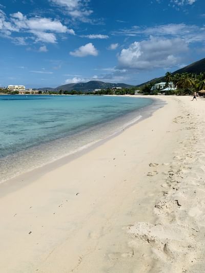 Wide sandy shoreline and clear ocean waters with distant green mountains in Lindbergh Bay Beach at Emerald Beach Resort