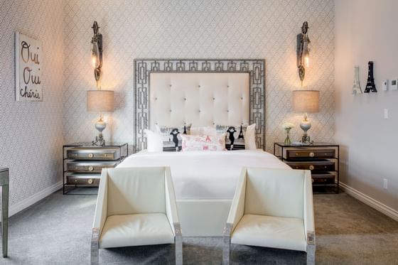 King bed with padded headboard, lamps & modern chairs in King Premiere Paris at Retro Suites Hotel