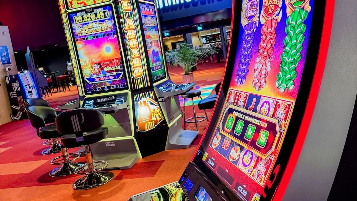 Machines à sous lumineuses dans un casino avec des sièges et un écran affichant 