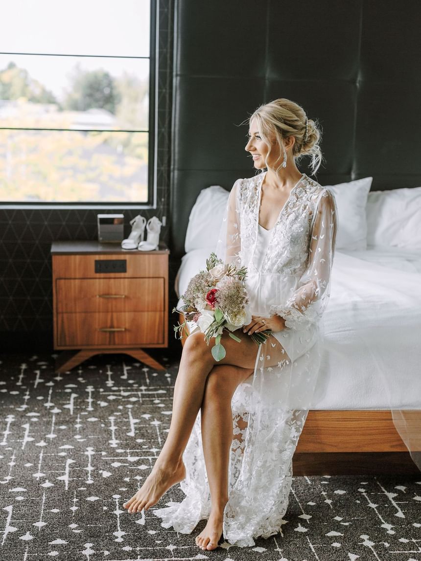 Bride with a flower bouquet smiling and sitting on cozy bed at The Earl