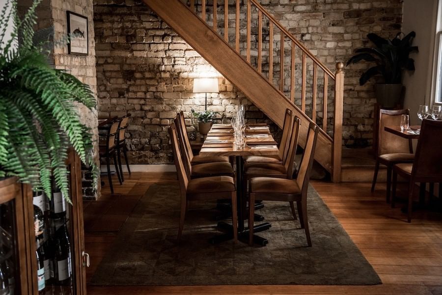 The dining room at Elysium Hotels has a rustic feel with brick walls and wooden stairs and tables with wine glasses