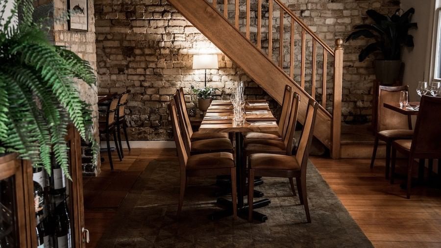 Dining table set under a rustic wooden staircase in The Herring Room at Elysium Manly, one of the best hotels in Manly