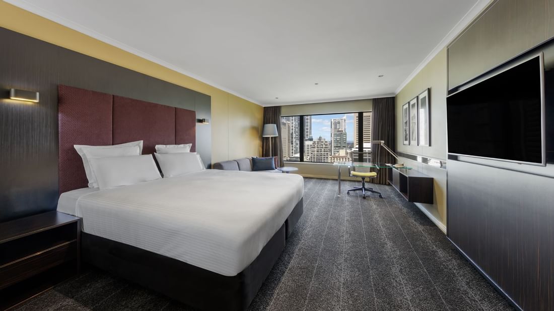 Comfy bed & lounge area overlooking the city in Deluxe Room at Pullman Sydney Hyde Park