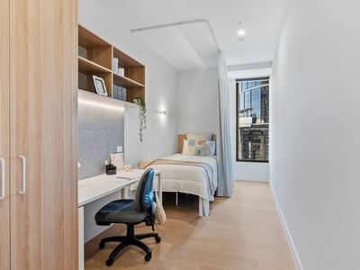 Modern single room with bed, desk, chair, and wooden closet at UniLodge Brisbane City.