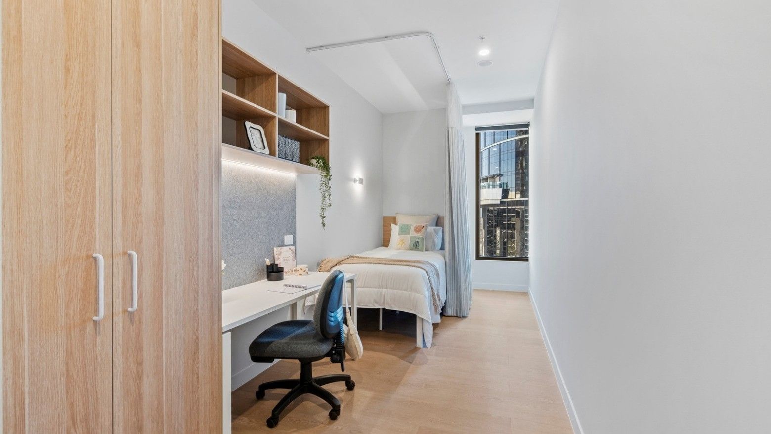Modern single room with bed, desk, chair, and wooden closet at UniLodge Brisbane City.