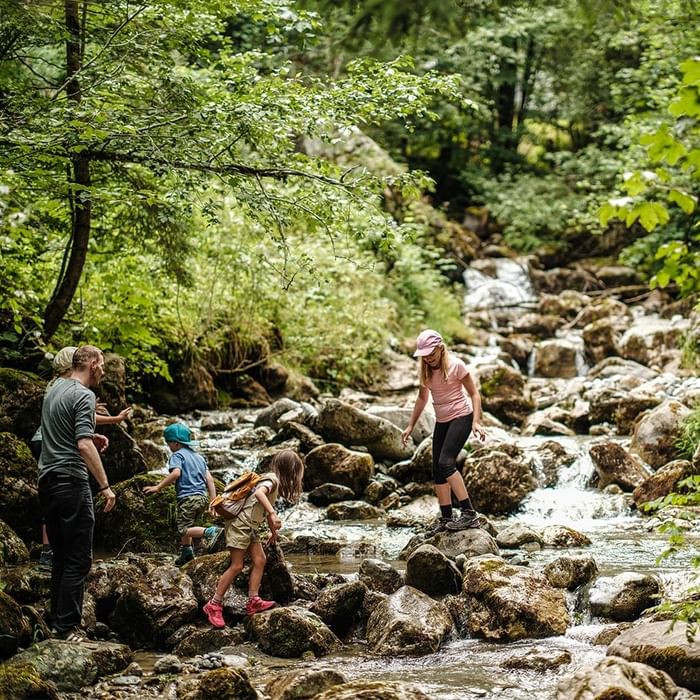 Family crossing a rocky stream in the forest near Falkensteiner Hotel Montafon