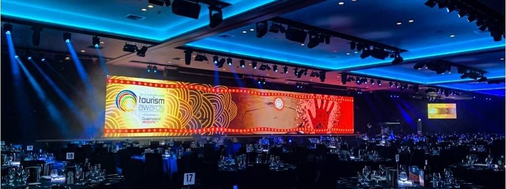Elegant venue set for the Queensland Tourism Awards with a vibrant stage & arranged tables at Novotel Sunshine Coast Resort