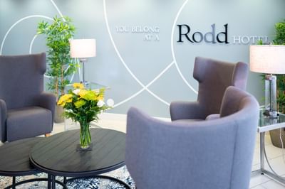 Grey armchairs around a dark wood coffee table with a yellow flower bouquet in the modern lobby at Rodd Moncton