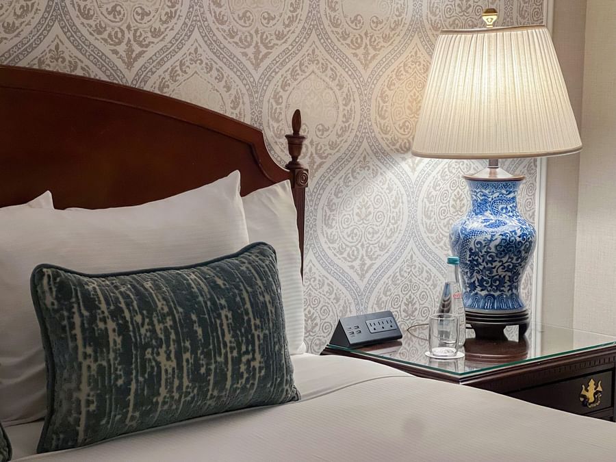 Elegant hotel room with a patterned wall, bedside table, and a lamp at Warwick New York.