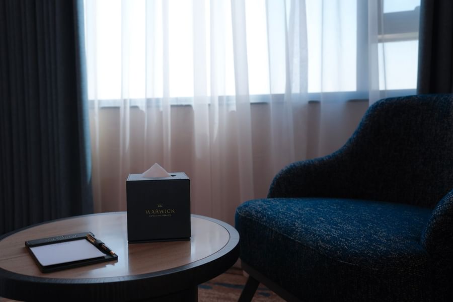 Tissue box and notebook on a round table next to a blue chair at Warwick Hotel & Spa - Jeddah.