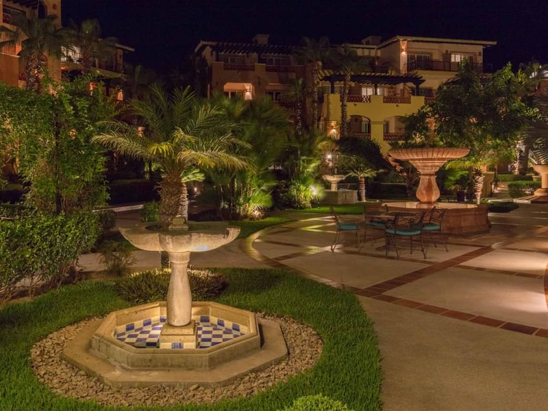 Hacienda Del Mar Los Cabos courtyard with multiple lit fountains, manicured gardens, and a small dining table at night 