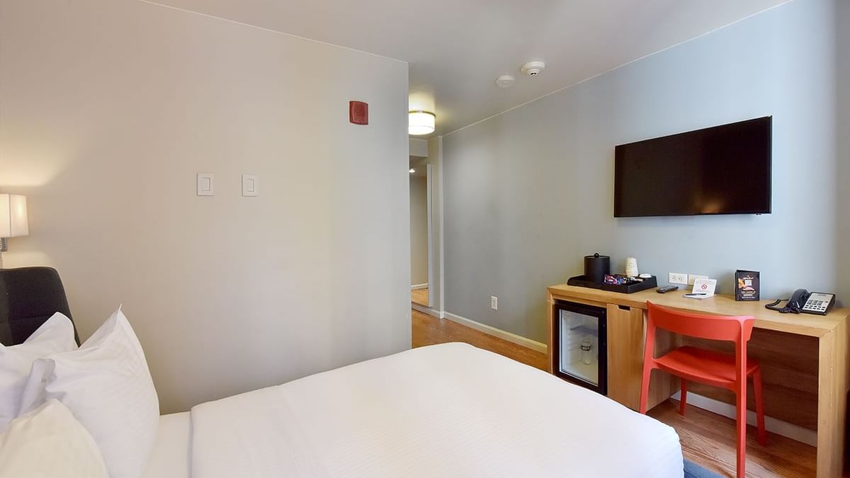 A hotel room with a king-size bed, desk, TV, mini fridge, and telephone.