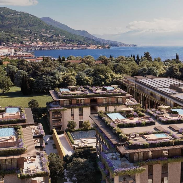 Aerial view of luxury buildings with rooftop pools, surrounded by lush greenery and overlooking a serene lake.