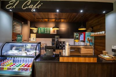 El Cafe coffee shop interior featuring menu boards and an espresso machine on a wood counter in Hotel Mirra