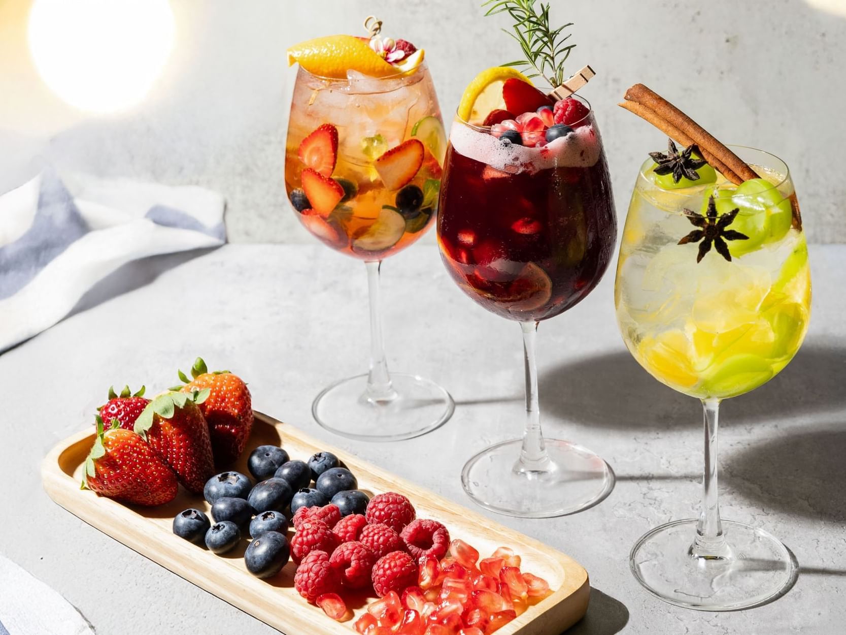 Three elegant glasses of wine surrounded by an assortment of fresh fruit and vibrant berries on a wooden table.