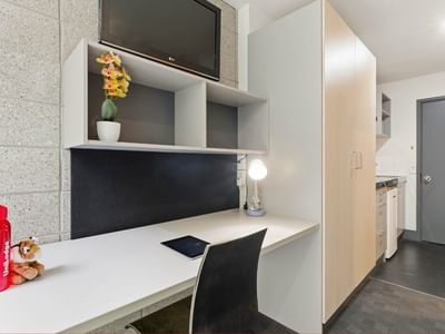 Student Living Auckland Beach room with desk, chair, TV, and flowers.