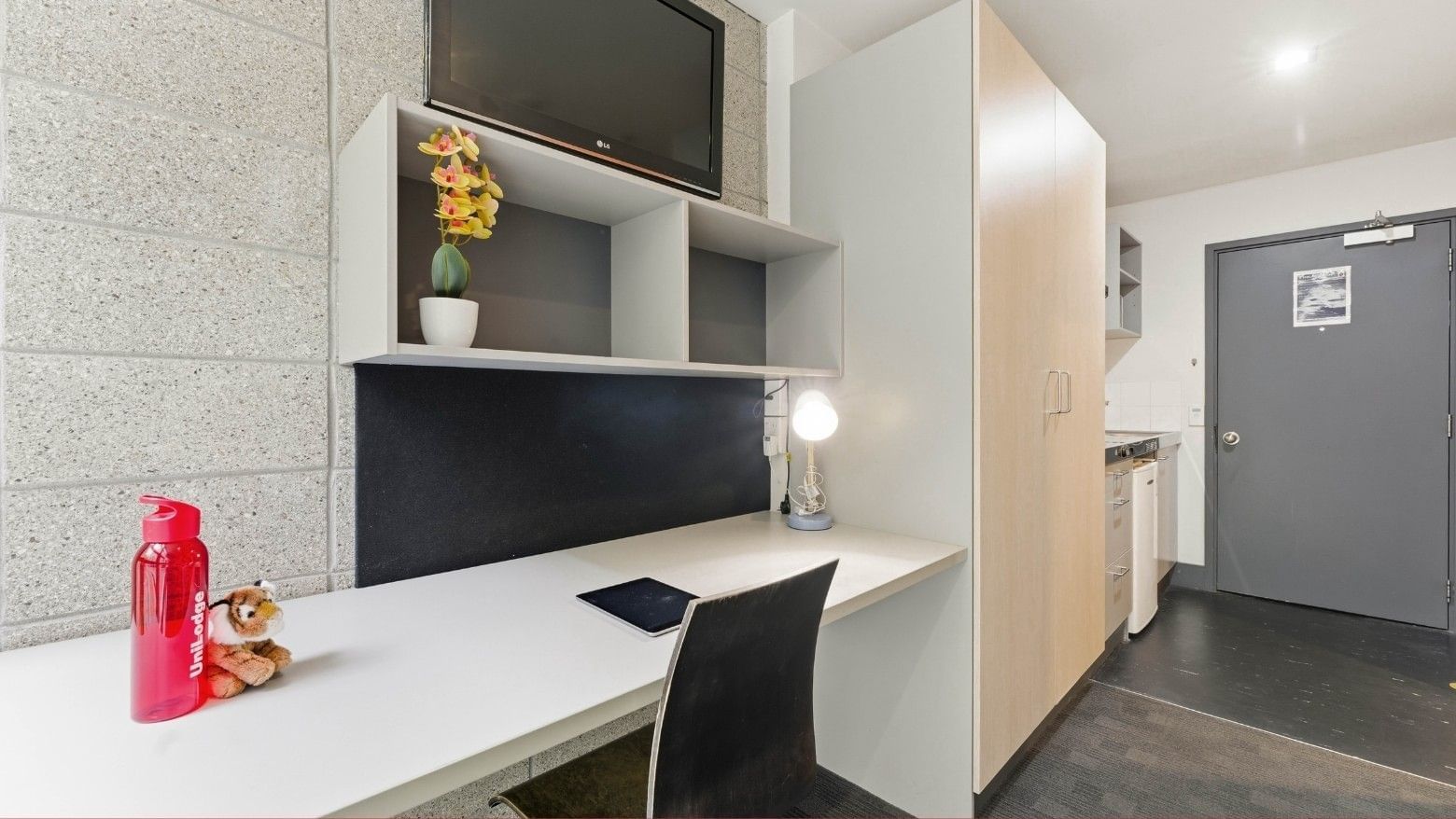 Modern room with desk, chair, flat screen TV, and storage at Student Living Auckland - Beach.