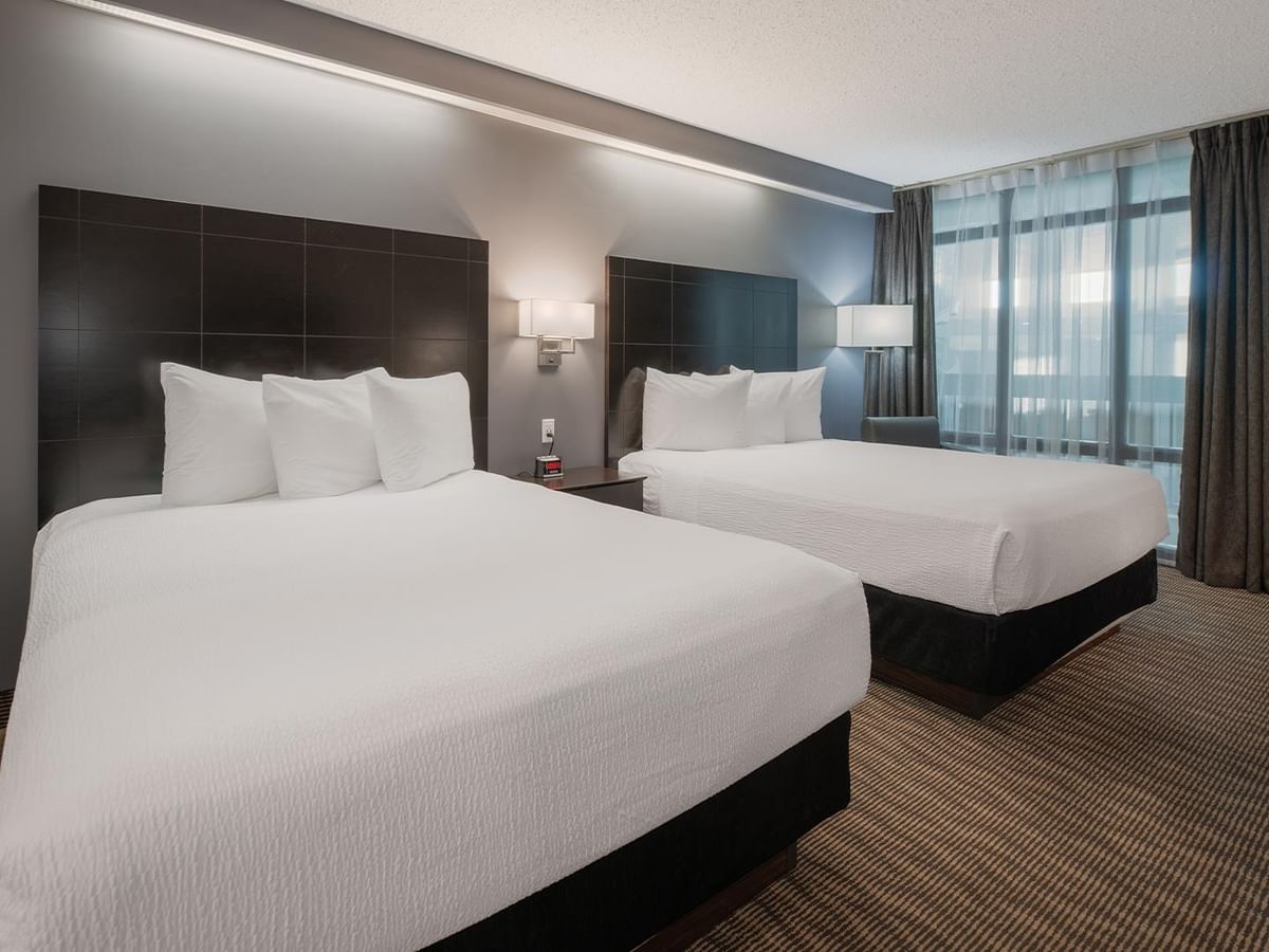 Two queen beds with white linens in a hotel room.