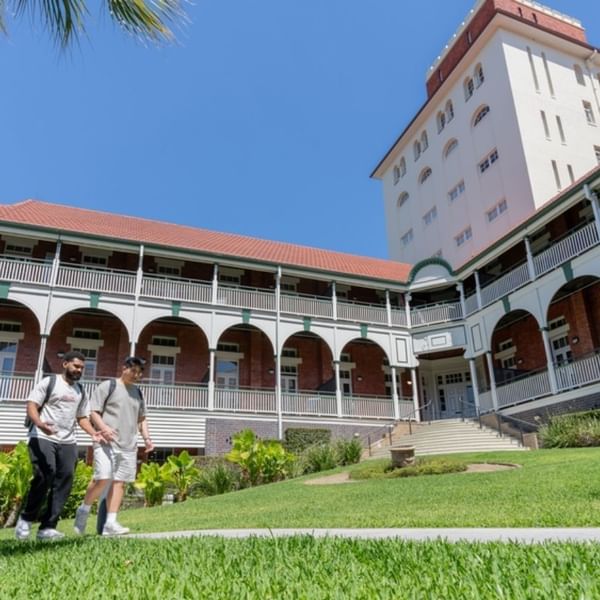 Two students walking in front of UniLodge Herston building surrounded by greenery.