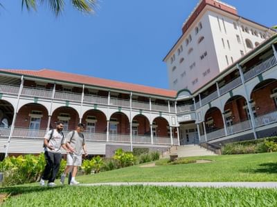 Two students walking in front of UniLodge Herston building surrounded by greenery.