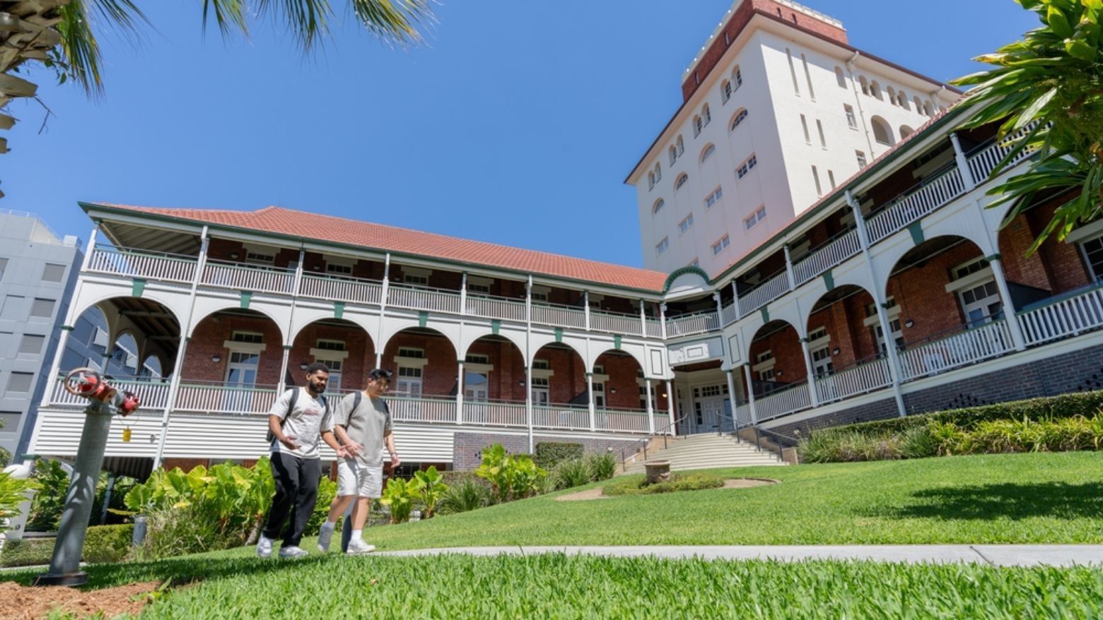 Two students walking in front of UniLodge Herston building surrounded by greenery.