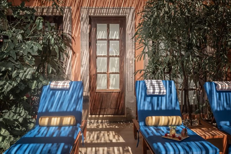 Outdoor seating with four blue lounge chairs facing a rustic wooden door amid lush greenery at Hacienda del Mar Los Cabos