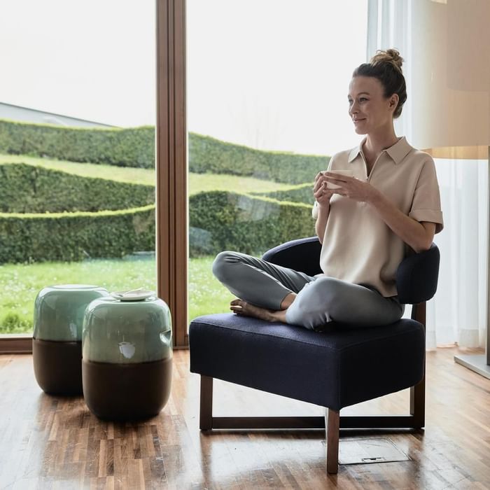 A woman sitting on a chair by a window holding a mug at Falkensteiner Balance Resort Stegersbach