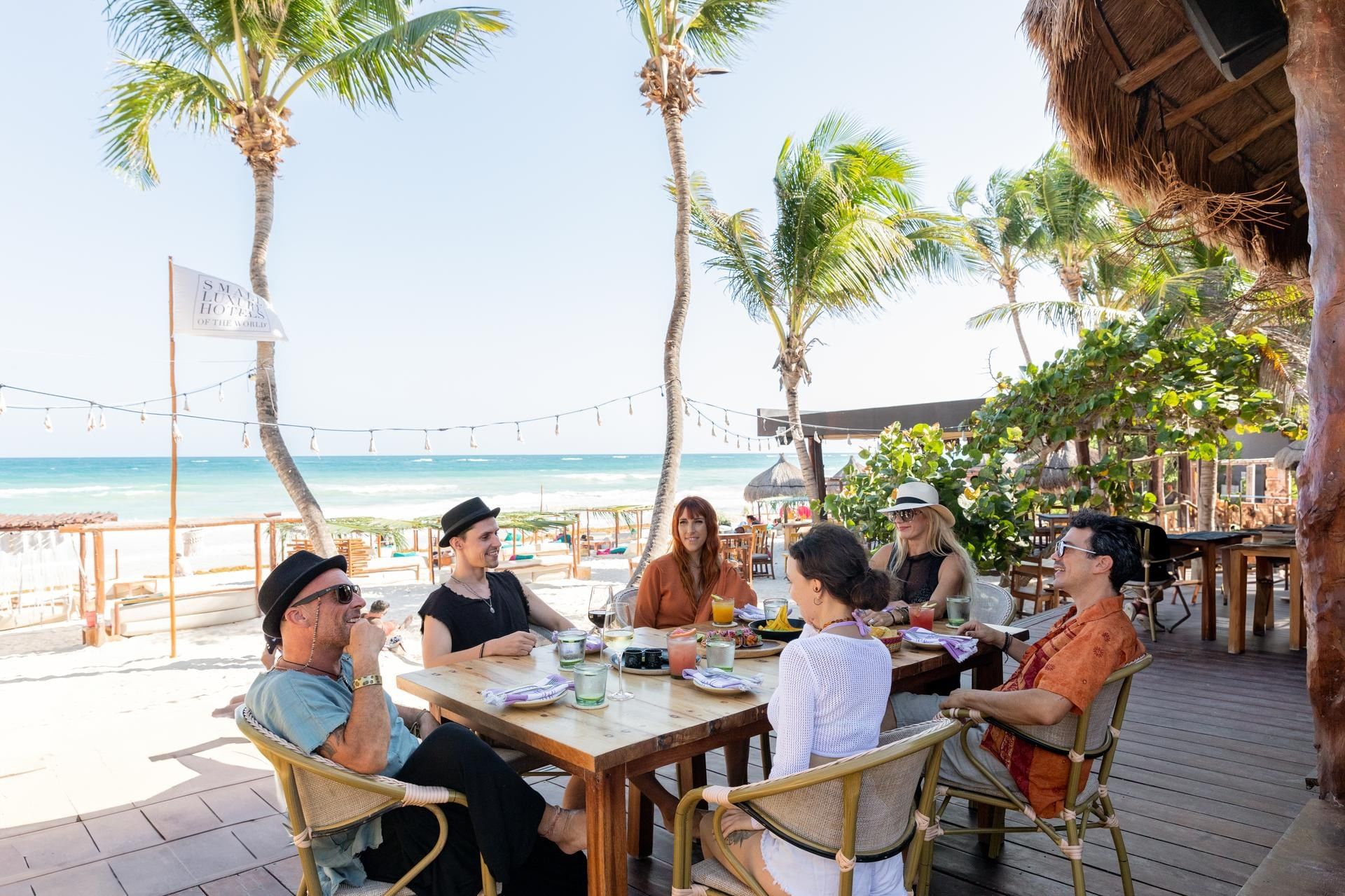 Friends sharing lunch at La Zebra’s beachfront restaurant, with palms and the Caribbean beyond the table.