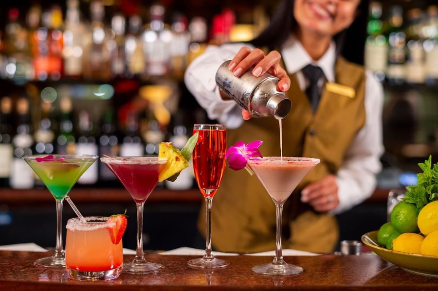 Smiling bartender pours a drink into one of five colorful, garnished cocktails at Warwick New York