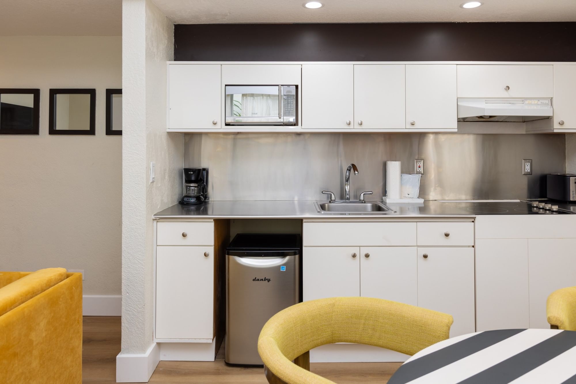 A kitchenette with white cabinets, stainless steel appliances, and yellow chairs.