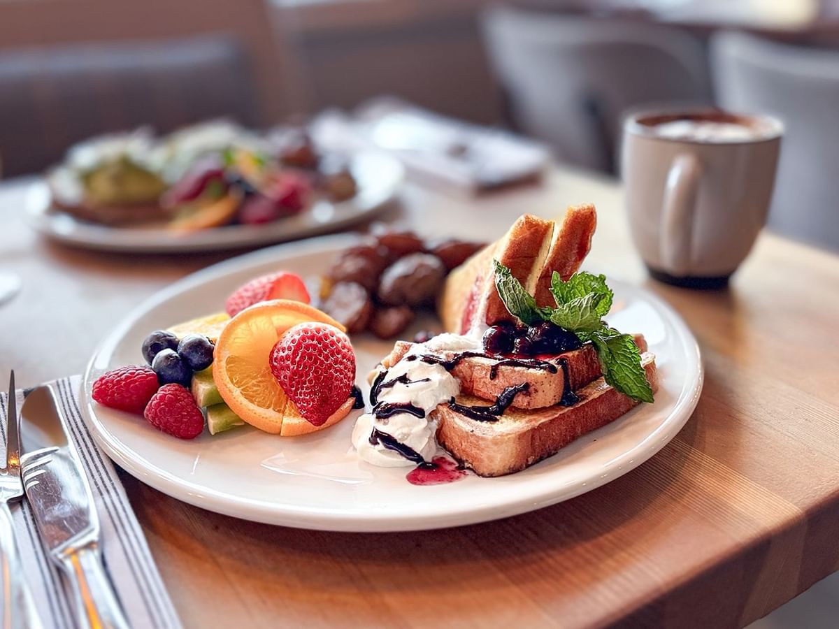 Plate of French toast with fruit and syrup, with coffee and orange juice on a table.