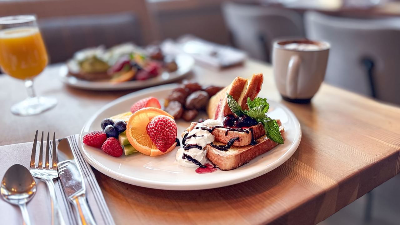Plate of French toast with fruit and syrup, with coffee and orange juice on a table.