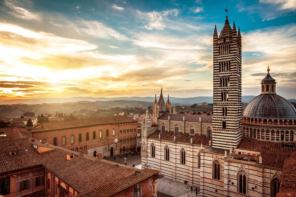 Cathedral of Santa Maria Assunta bell tower & historic cityscape under warm golden sunset sky near Meraviglia