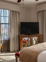 Flat-screen TV on a wooden stand by a chair under drapes in Corner King at Warwick Melrose Dallas