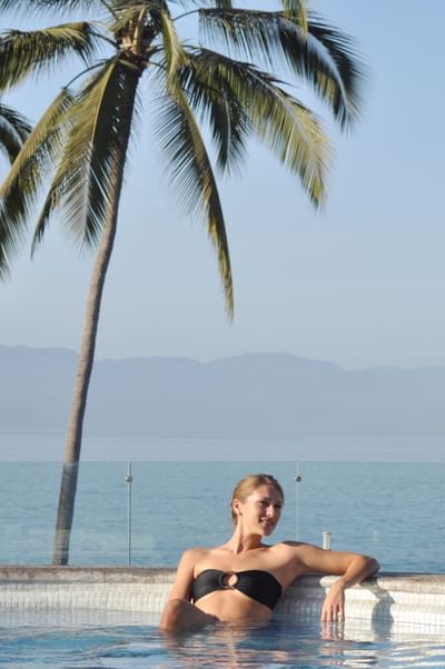 Foto del hotel Sunset Plaza Beach Resort que muestra a una mujer relajándose en la piscina con bañador negro, palmeras y montañas de fondo