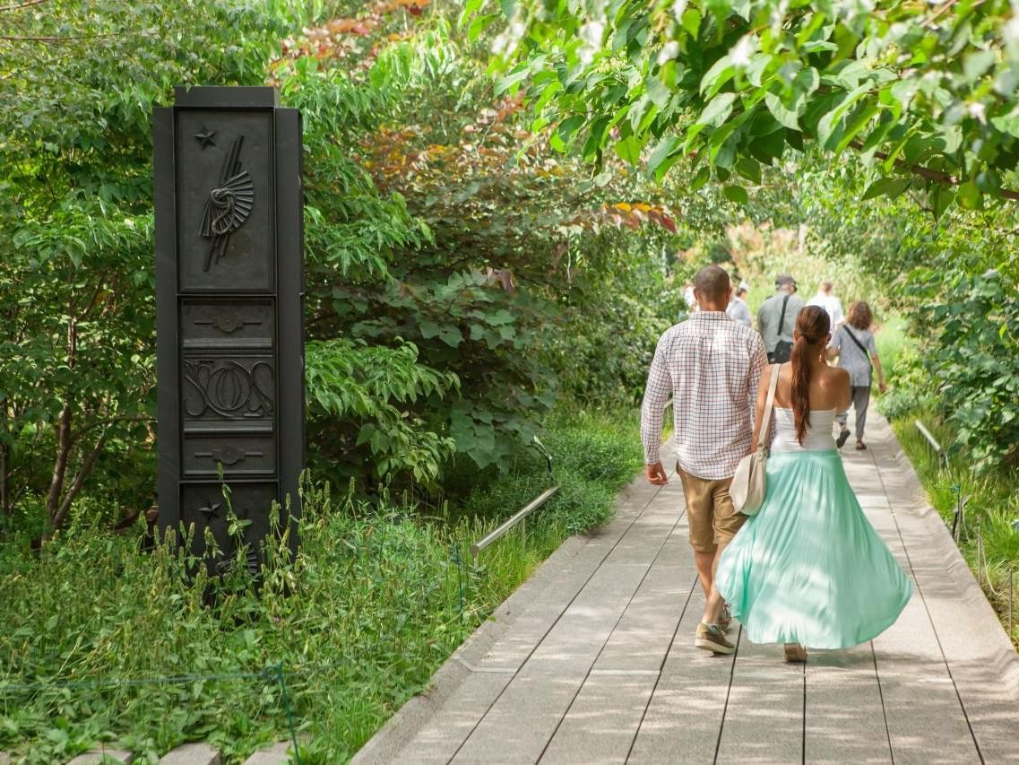 Couples stroll along a The High Line in Chelsea Manhattan surrounded by lush greenery.