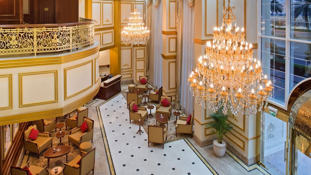 Striped armchairs by small coffee tables under massive crystal chandeliers in the lobby at Warwick Doha Hotel