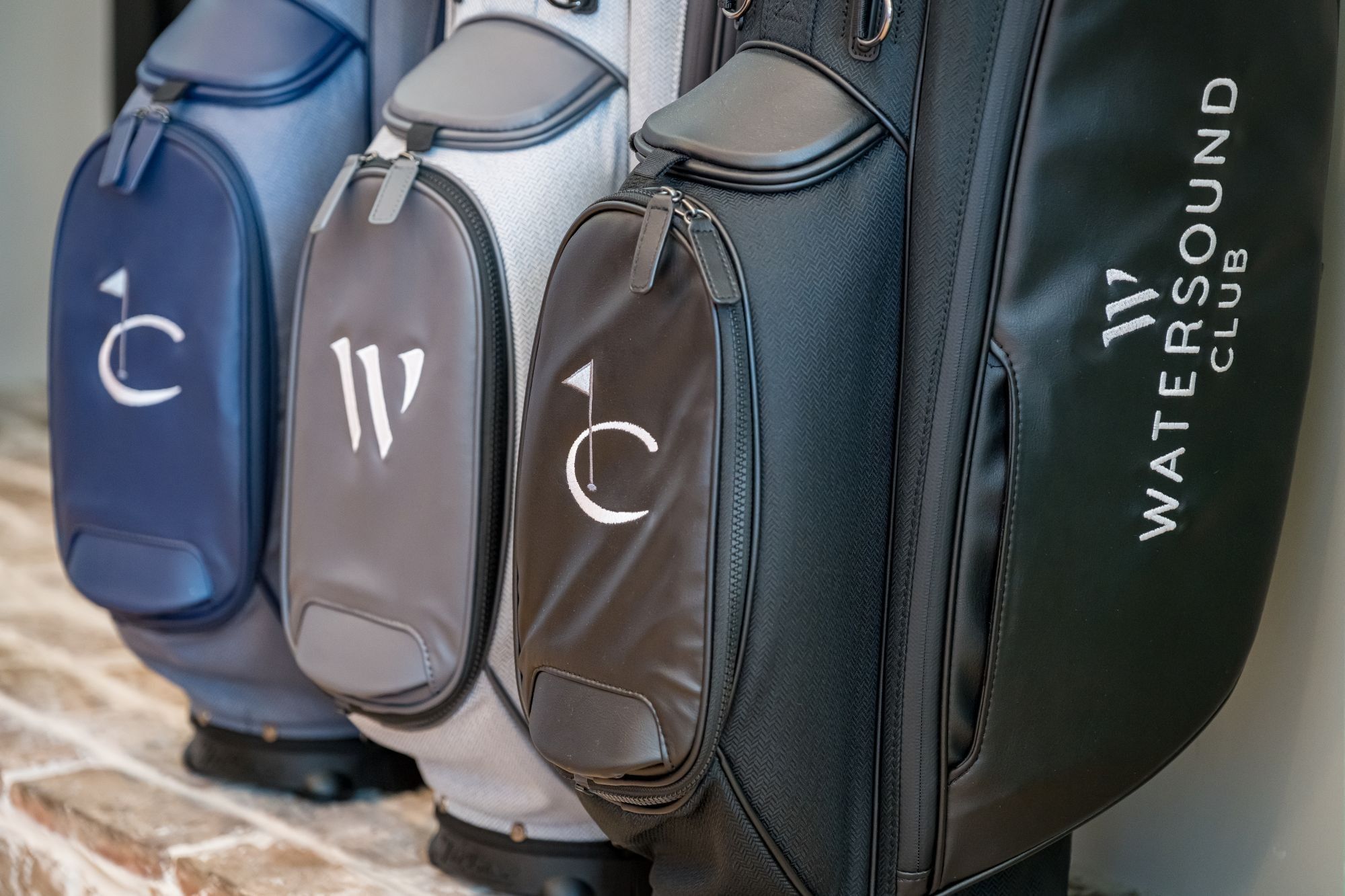 Golf bags in blue, gray, and green with white monogram letters displayed on a stone ledge at Camp Creek Inn