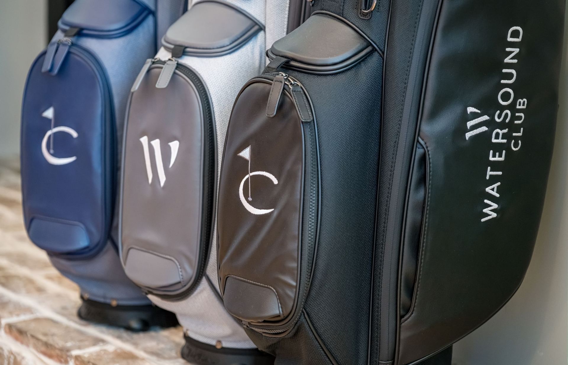Golf bags in blue, gray, and green with white monogram letters displayed on a stone ledge at Camp Creek Inn